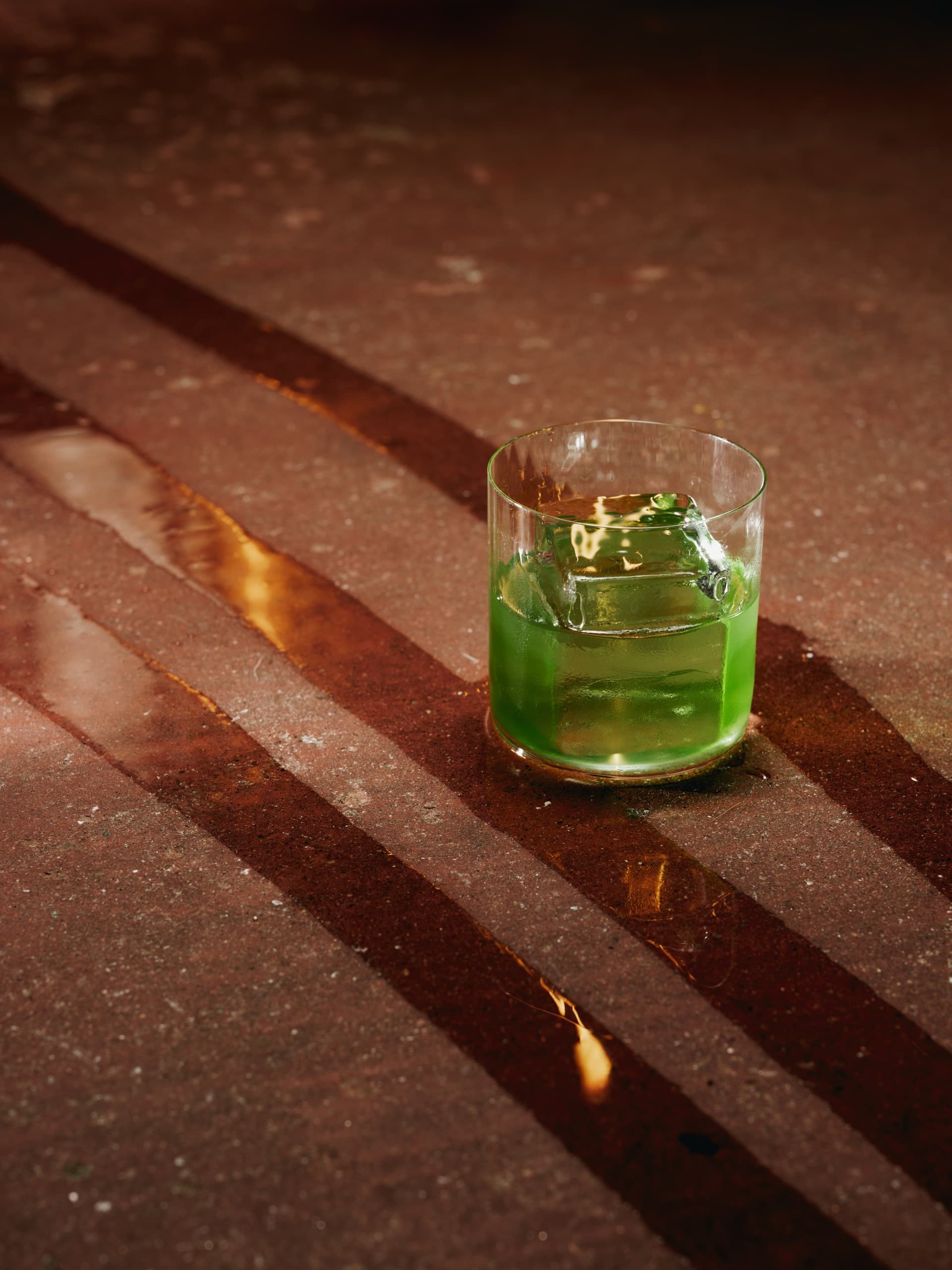 Grön cocktail med stor isbit på stenbord